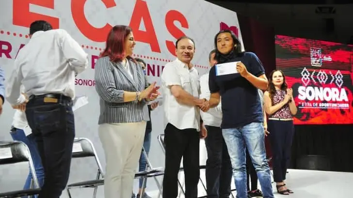 Un estudiante seri recibe la beca educativa de manos del gobernador Alfonso Durazo Montaño.